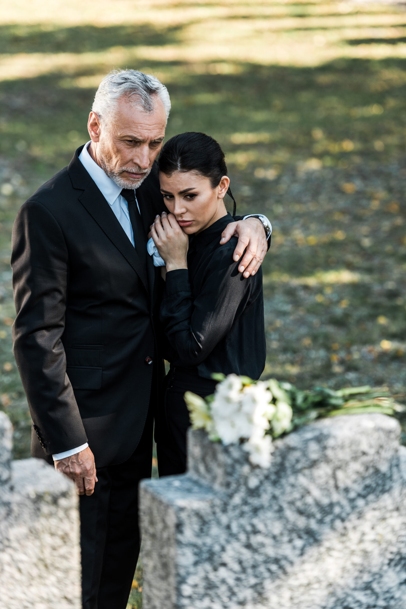 selective focus of senior man hugging upset woman on graveyard
